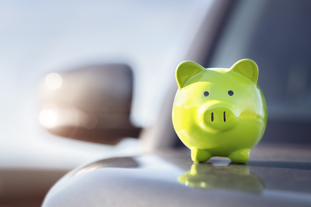 Grünes Sparschwein auf der Motorhaube eines silbernen Autos.