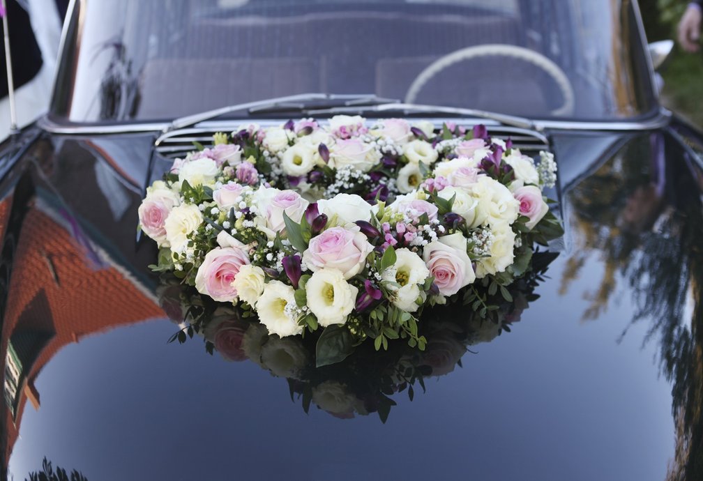 Hochzeitsauto mit großem Blumenschmuck auf der Motorhaube.