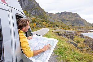 Person schaut im Camper auf eine Landkarte und plant die Route entlang einer kurvigen Straße in bergiger Landschaft.
