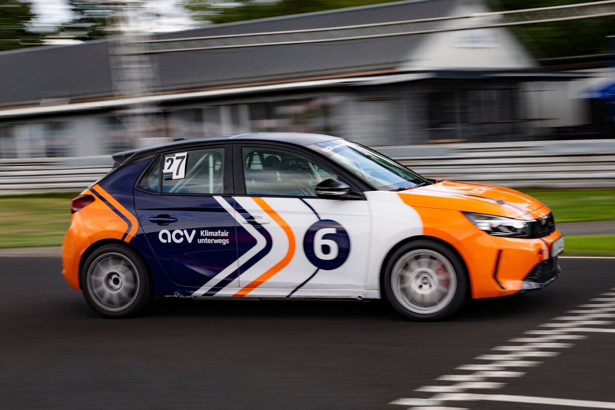 Ein Rennwagen mit der Startnummer 6 und einer orange-weiß-blauen Lackierung rast über eine Rennstrecke, wobei der unscharfe Hintergrund die Bewegung verdeutlicht.