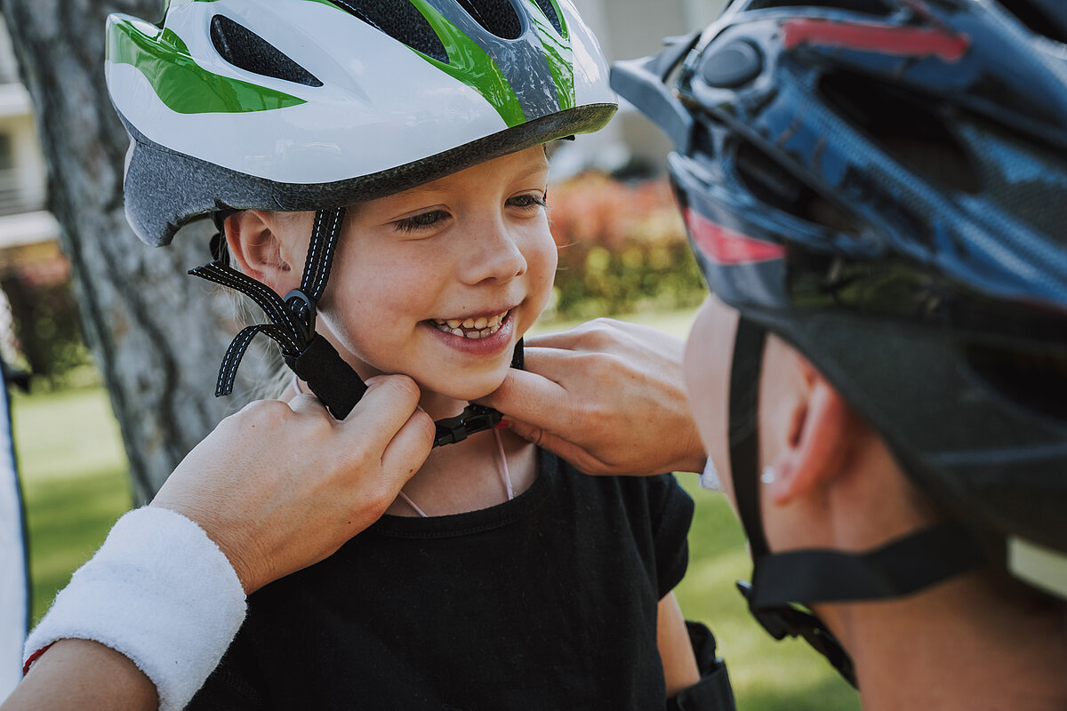 Mutter zieht ihrem Kind einen Fahrradhelm an