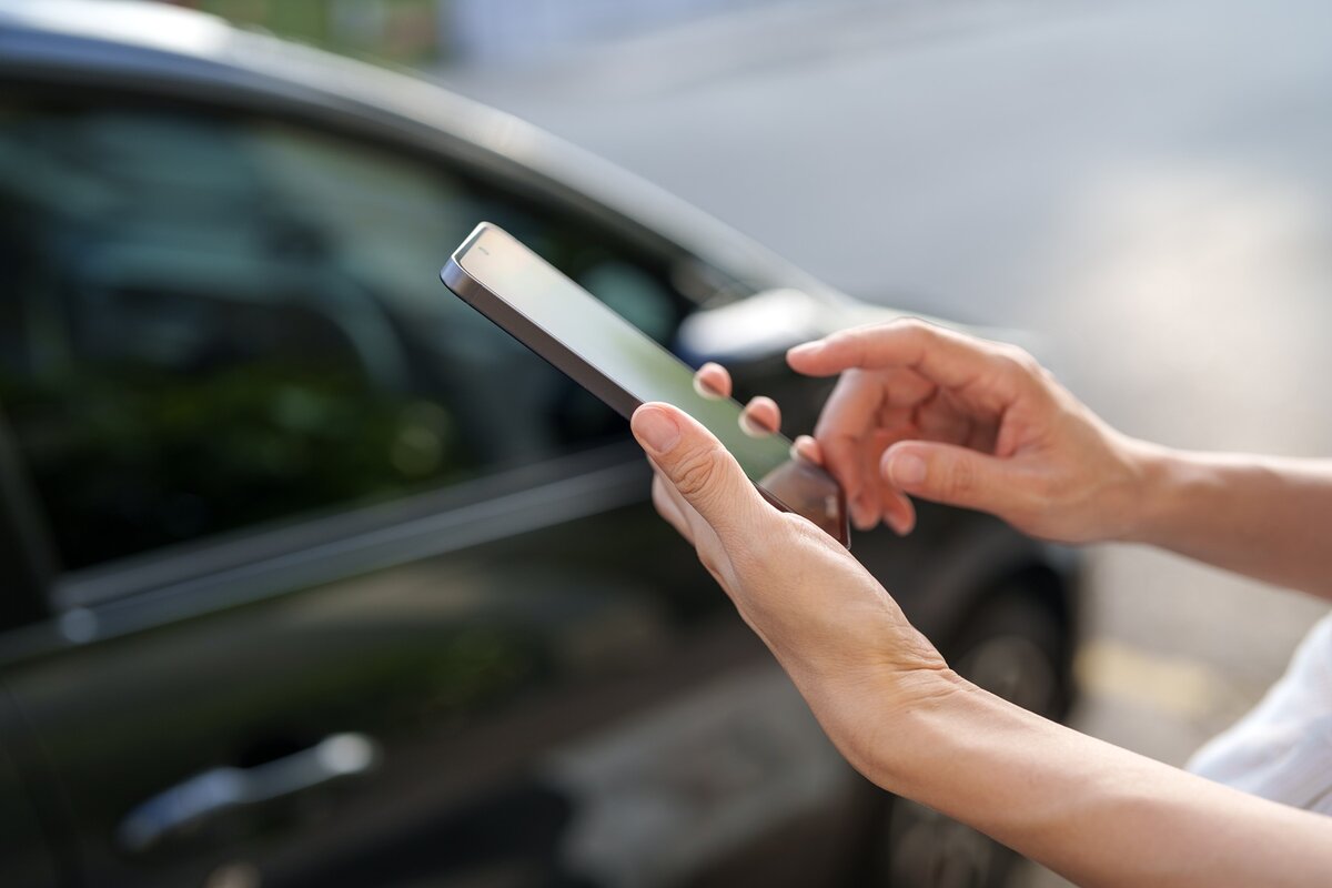 Eine Person benutzt tagsüber ihr Smartphone, während sie neben einem geparkten Auto auf der Straße steht.