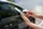 Eine Person benutzt tagsüber ihr Smartphone, während sie neben einem geparkten Auto auf der Straße steht.