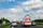 Ein Krankenwagen mit Blaulicht fährt auf einer Autobahn und überholt unter einem teilweise bewölkten Himmel Autos und andere Fahrzeuge. Im Hintergrund säumen Bäume die Straße.
