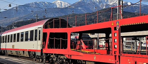 Ein Autoreisezug fährt auf Schienen an Bergen vorbei