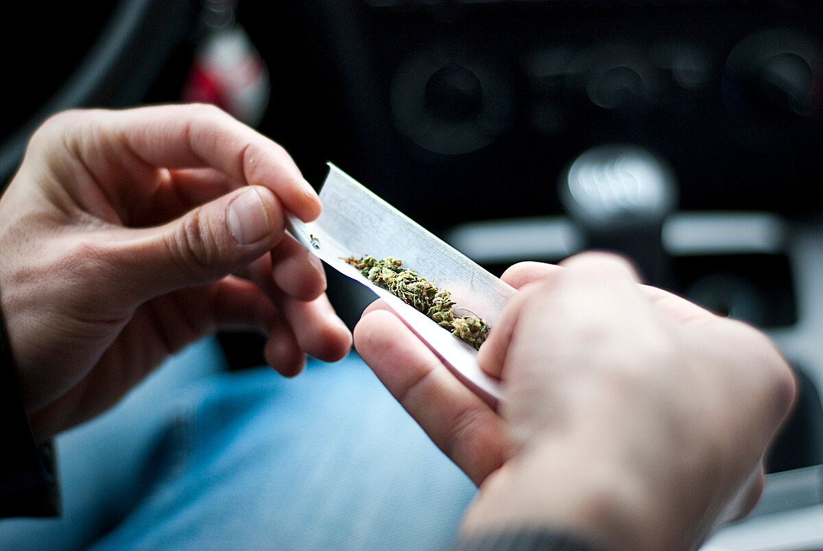 Mann in einem Auto dreht einen Joint