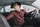 Junger Mann mit Brille und rotem Langarmshirt sitzt am Steuer eines Autos, dreht sich nach hinten und blickt konzentriert über die rechte Schulter – typische Szene beim Einparken.