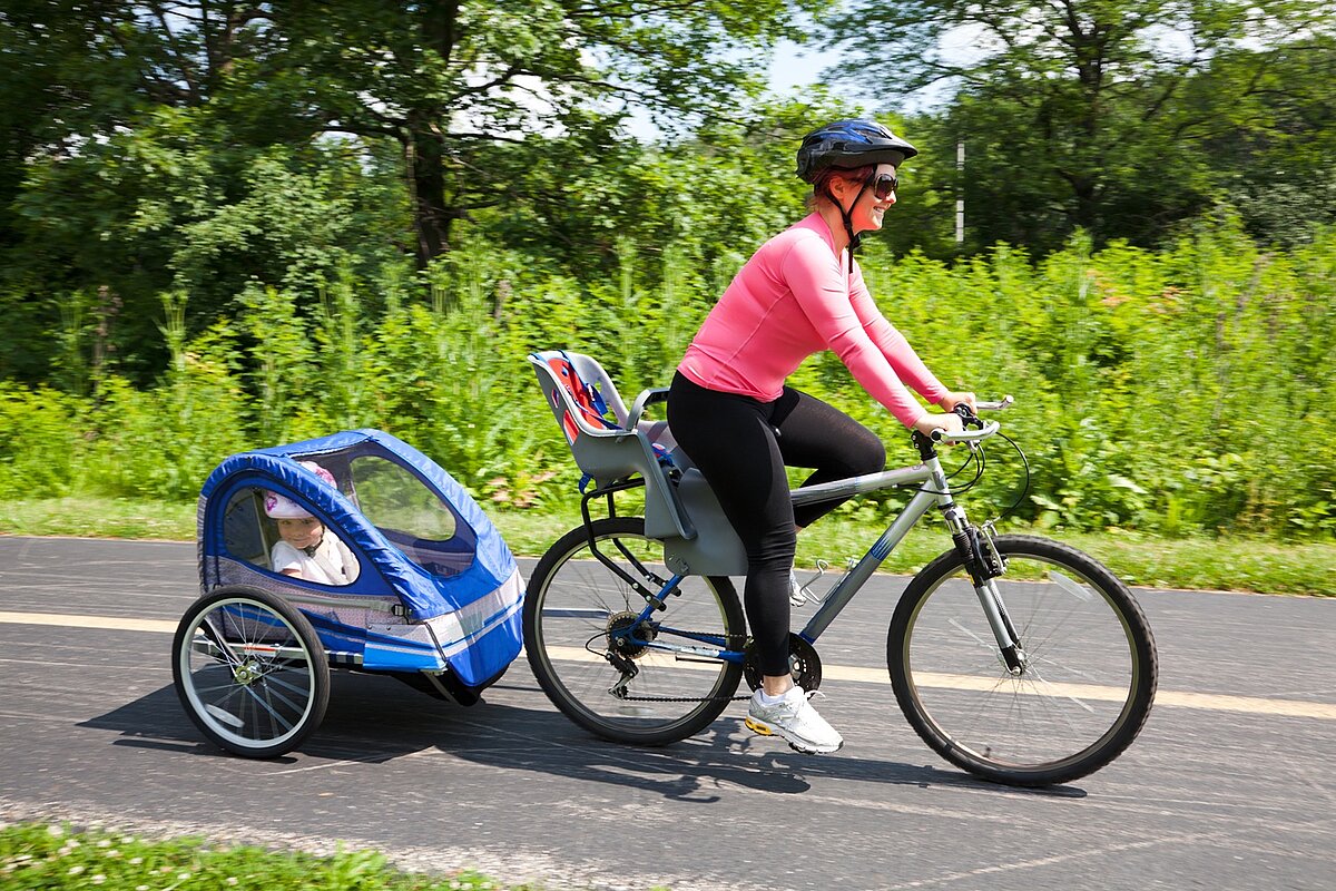 Frau transportiert Kind im Fahrradanhänger auf einem Radweg.