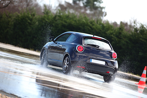 Ein Fahrzeug fährt dynamisch über nassen Asphalt an einem Pylon vorbei