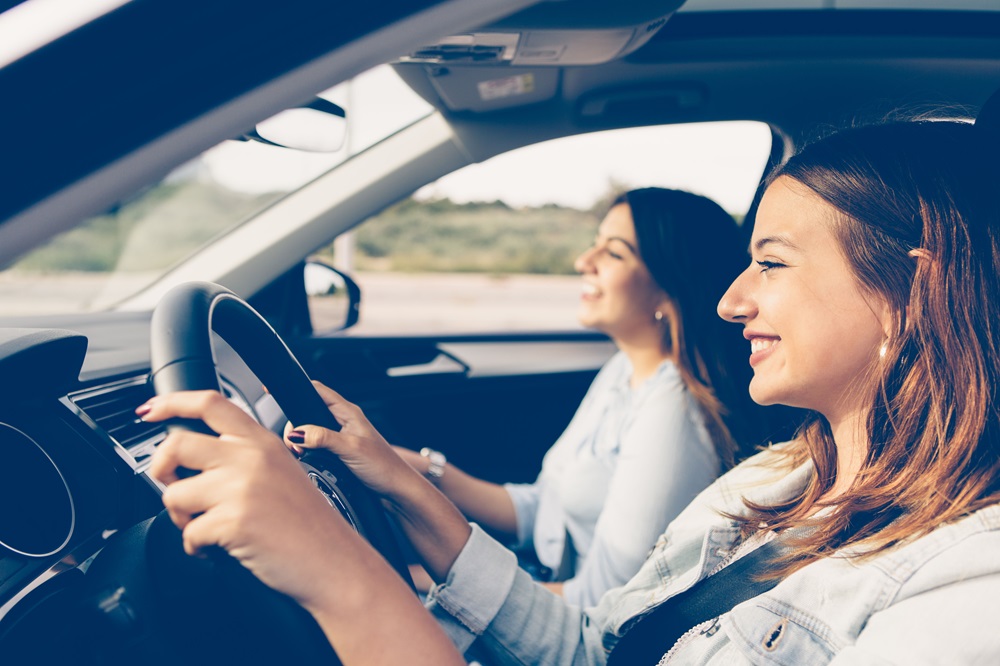 2 junge Frauen sitzen lächelnd in einem Fahrzeug