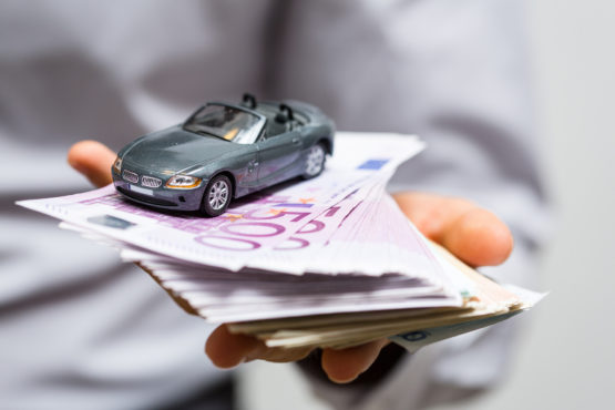 Ein Mann hält Geld und ein kleines Auto in der Hand