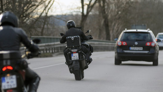 2 Motorradfahrer fahren auf einer Straße hinter Autos