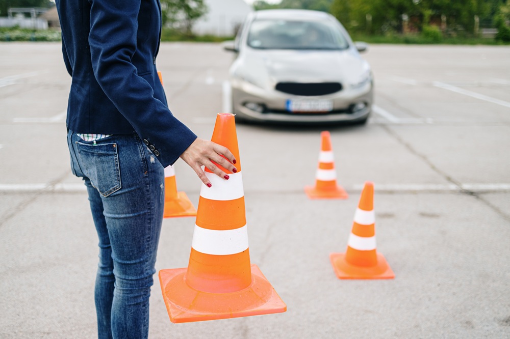 Vater stellt Verkehrskegel auf einem Parkplatz auf, während sein Sohn mit dem Auto das Einparken übt.
